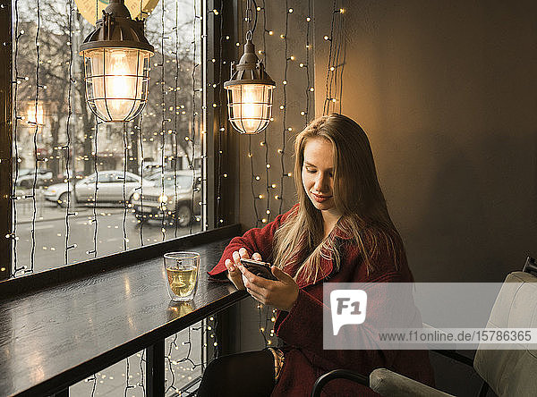 Young woman with cup of tea sitting in a coffee shop using mobile phone