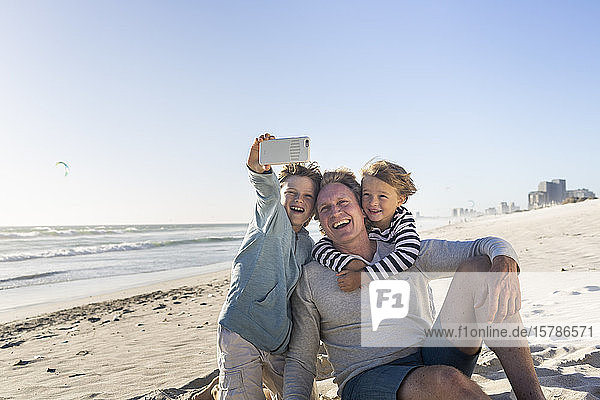Father having fun with his sons on the beach  taking smartphone pictures
