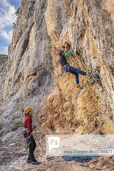 Woman securing man climbing at rock face