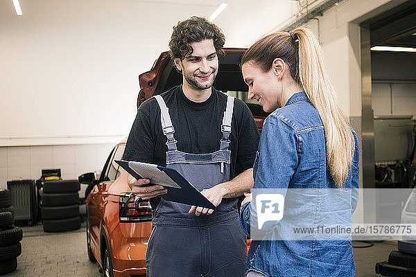 Automechaniker zeigt dem Kunden in der Werkstatt die Checkliste