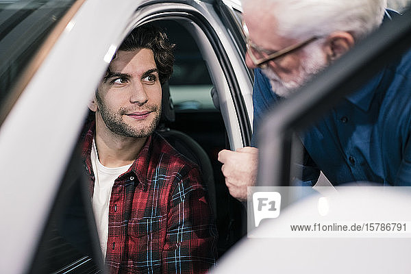 Autohändler zeigt Auto einem jungen Mann im Ausstellungsraum
