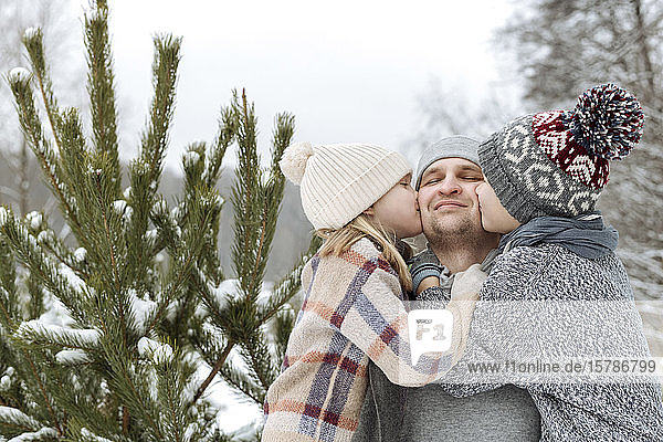 Two kids kissing their happy father at a fir tree in winter