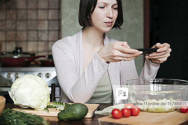 Porträt einer Frau  die einen Salat mit einem Smartphone fotografiert