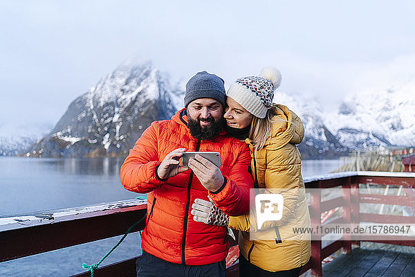 Tourist couple using smartphone at Hamnoy  Lofoten  Norway