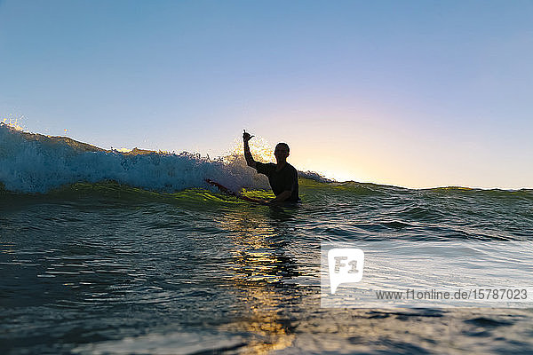 Surfer making surfer sign sitting on surfboard Bali Indonesia