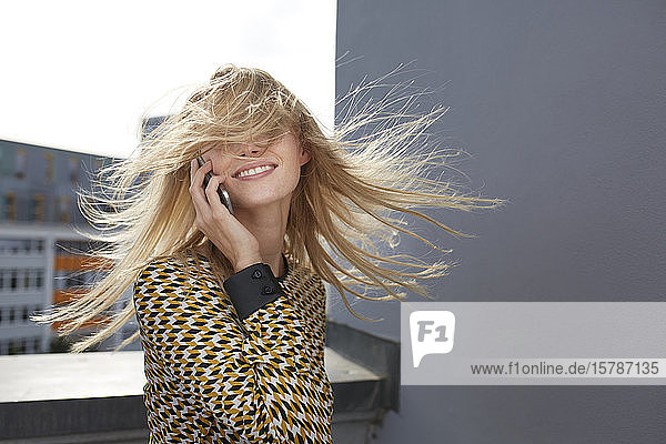 Lächelnde blonde junge Frau mit windgeblasenem Haar am Telefon