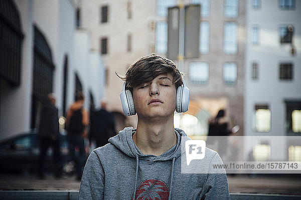 Portrait of teenager with headphones  sitting on steps in the city