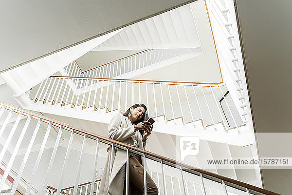 Young woman with smartphone walking down stairs in staircase
