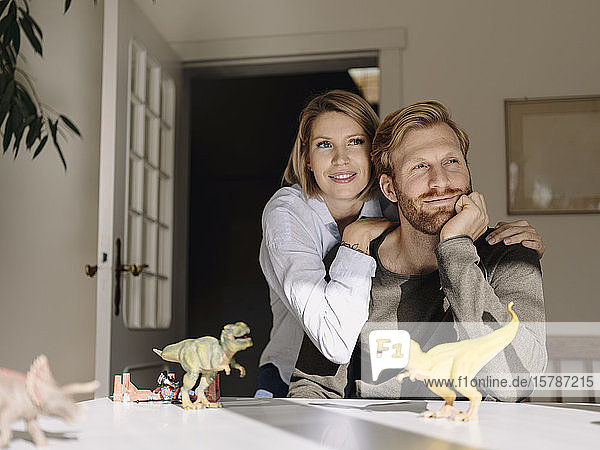 Smiling couple sitting at table at home with toy dinosaurs