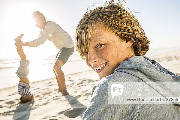 Portrait of smiling boy with father helping son doing a headstand on the beach in background