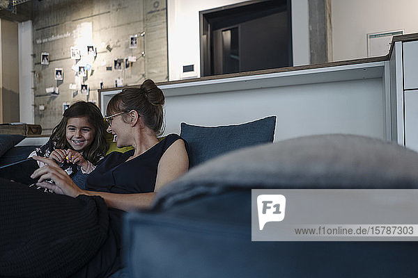 Happy woman and girl sitting on couch in office using smartphone