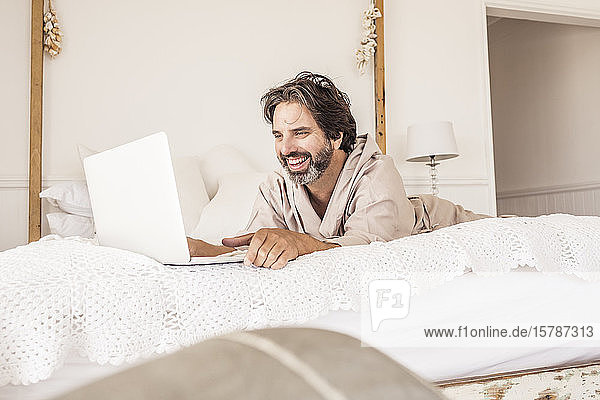 Mann im Bademantel  im Schlafzimmer auf dem Bett liegend  mit Laptop