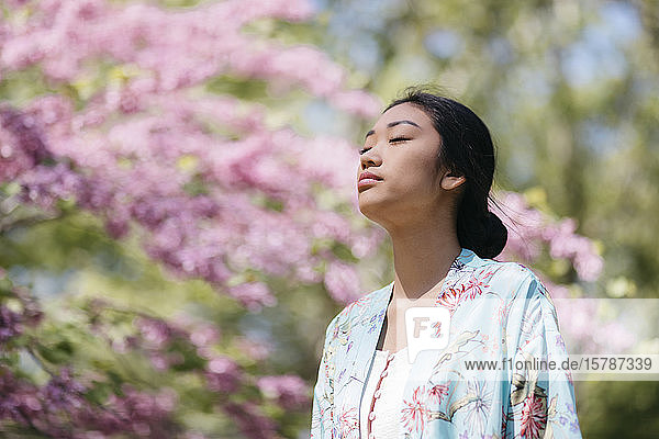 Hübsche junge Frau mit blühendem Kirschbaum in einem öffentlichen Garten im Frühling