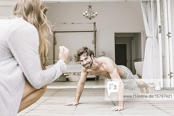 Young woman encouraging man doing pushups in bedroom