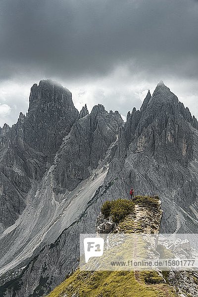 Mann mit roter Jacke steht auf einer Stufe  hinter ihm Berggipfel und spitze Felsen  dramatische Wolken  Cimon die Croda Liscia und Cadini Gruppe  Auronzo di Cadore  Belluno  Italien  Europa