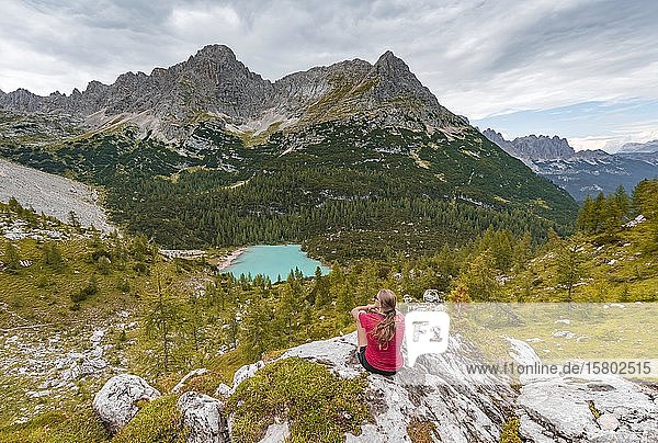 Young woman  hiker sitting on rocks and looking at turquoise green Sorapiss lake and mountain landscape  Dolomites  Belluno  Italy  Europe