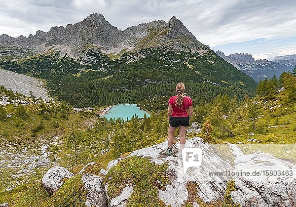 Young woman  hiker stands on rocks and looks at turquoise green Sorapiss lake and mountain landscape  Dolomites  Belluno  Italy  Europe