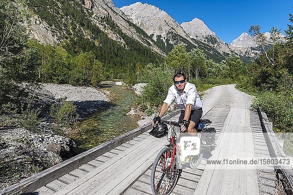 Cyclist  mountain biker bikes on bridge over mountain stream  gravel path to Karwendelhaus  Karwendel valley  Tyrol  Austria  Europe
