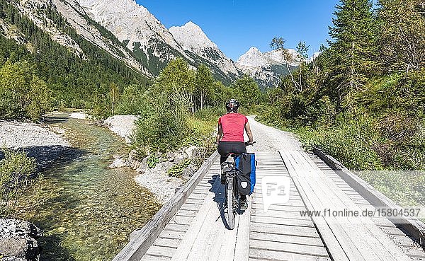 Cyclist  mountain biker bikes on bridge over mountain stream  gravel path to Karwendelhaus  Karwendeltal  Tyrol  Austria  Europe