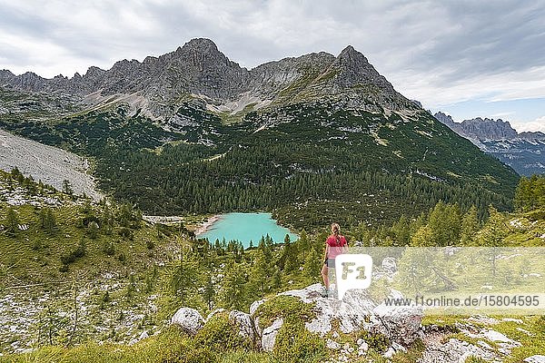 Junge Frau  Wanderer steht auf Felsen und schaut auf den türkisgrünen Sorapiss-See und die Berglandschaft  Dolomiten  Belluno  Italien  Europa