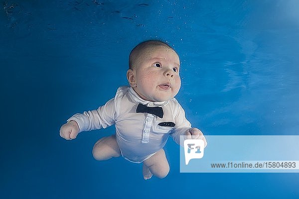 Kleiner Junge in weißem Anzug und Fliege schwimmt unter Wasser  Russland  Europa