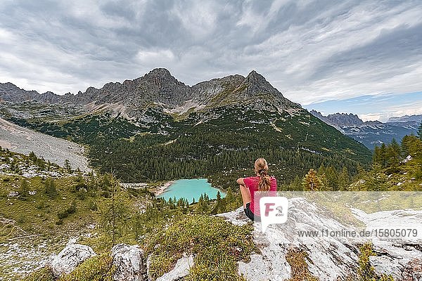 Junge Frau  Wanderer auf Felsen sitzend mit Blick auf türkisgrünen Sorapiss-See und Berglandschaft  Dolomiten  Belluno  Italien  Europa