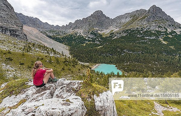 Young woman  hiker sitting on rocks and looking at turquoise green Sorapiss lake and mountain landscape  Dolomites  Belluno  Italy  Europe