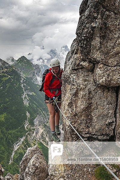 Young woman  hiker climbing a rock face in a via ferrata Vandelli  Sorapiss circuit  mountains with low clouds  Dolomites  Belluno  Italy  Europe
