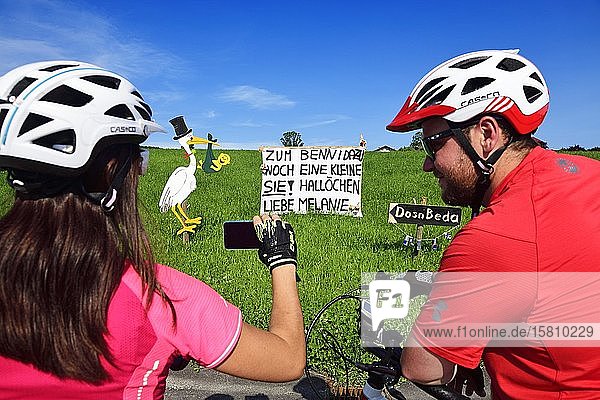 Radfahrer fotografieren Klapperstorch und Banner als Willkommensgruß für ein neugeborenes Kind  Seeham  Salzburger Seenland  Salzburger Land  Österreich  Europa