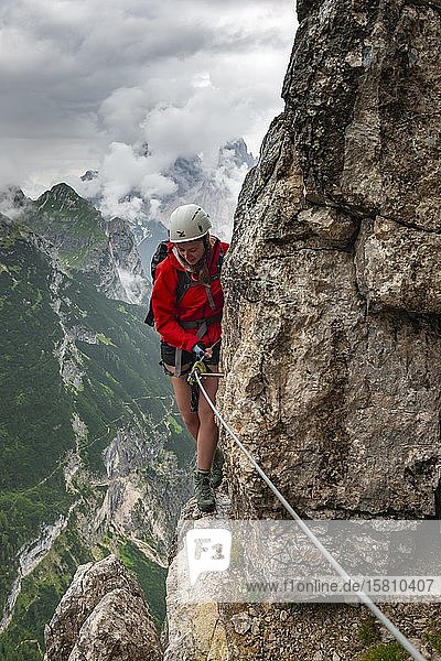Junge Frau  Wanderin  die eine Felswand im Klettersteig Vandelli erklimmt  Sorapiss-Rundweg  Berge mit niedrigen Wolken  Dolomiten  Belluno  Italien  Europa