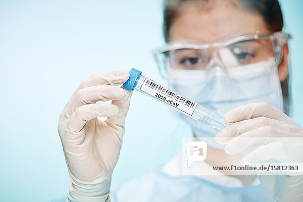Laborantin mit Schutzbrille und Mundschutz hält Probe mit Coronavirus in Kamera