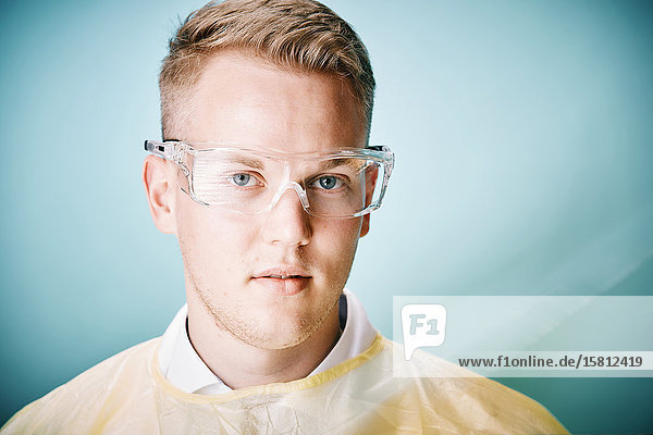 Junger Arzt mit Schutzbrille blickt in Kamera