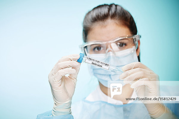Laborantin mit Schutzbrille und Mundschutz hält Probe mit Coronavirus in Kamera