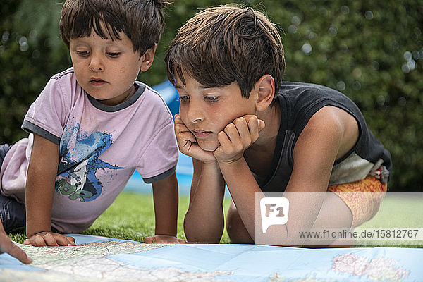 Two boys sitting outdoors on a lawn  looking at a world map.
