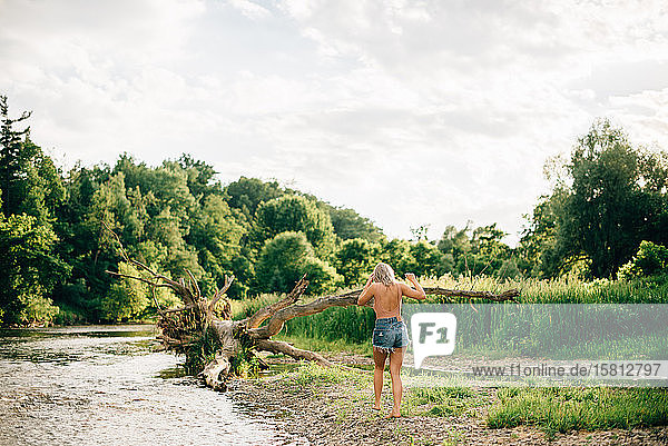 Rear view of young woman wearing shorts walking along a river bank.