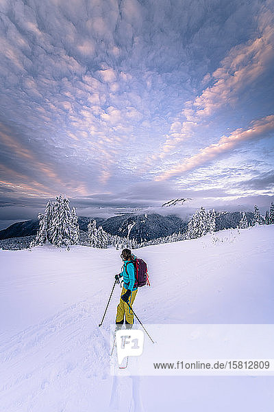 Person beim Skifahren durch eine winterliche Landschaft  Berge in der Ferne  dramatischer Himmel.