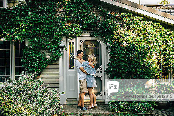 Young couple standing outside cottage  hugging and smiling at each other.