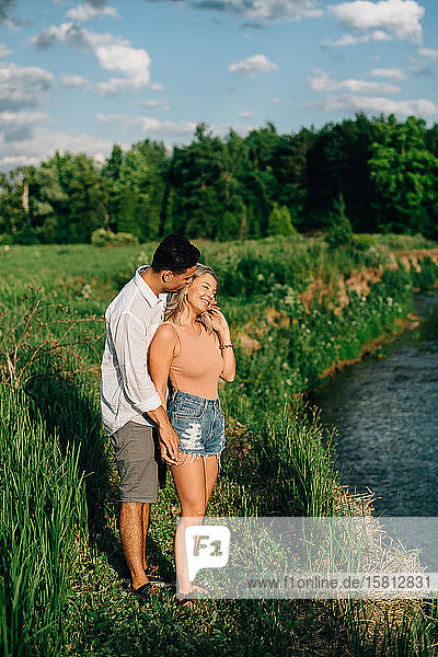 Young couple standing on a path by a river smiling and hugging.