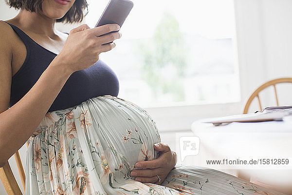 Schwangere Frau in geblümtem Kleid mit Smartphone