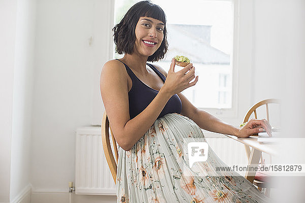 Porträt einer glücklichen schwangeren Frau  die Avocado-Toast isst