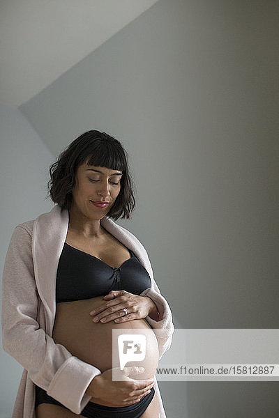 Schwangere Frau im BH hält Bauch