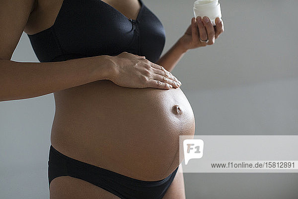 Close up schwangere Frau Anwendung Feuchtigkeitscreme auf den Bauch