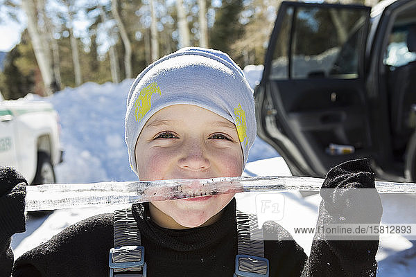 Lächelnder sechsjähriger Junge mit einem langen Eiszapfen im Mund