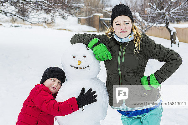 Bruder und Schwester  ein Junge und ein junges Mädchen lehnen sich im Winter an einen Schneemann