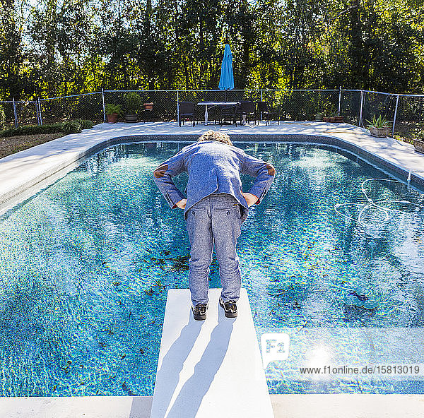 Ein sechsjähriger Junge steht auf einem Sprungbrett mit Blick auf den Pool