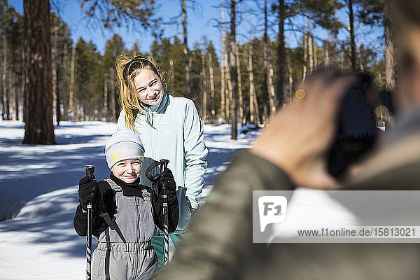 Mutter fotografiert ihre beiden Kinder  einen Jungen und ein Teenager-Mädchen  in verschneiter Waldlandschaft