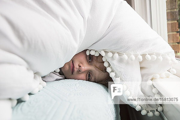 Ein sechsjähriger Junge im Bett mit Decken über dem Kopf