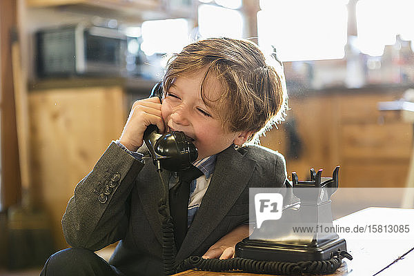 A six year old boy in a suit and tie talking on a old vintage phone at home