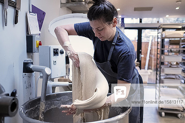 Frau mit Schürze  die in einer handwerklichen Bäckerei steht und mit Sauerteig arbeitet.