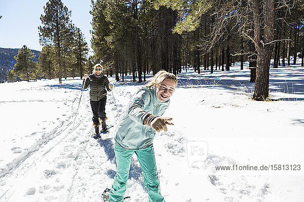 Thirteen year old girl and her mother on snow shoes on a trail in snow.